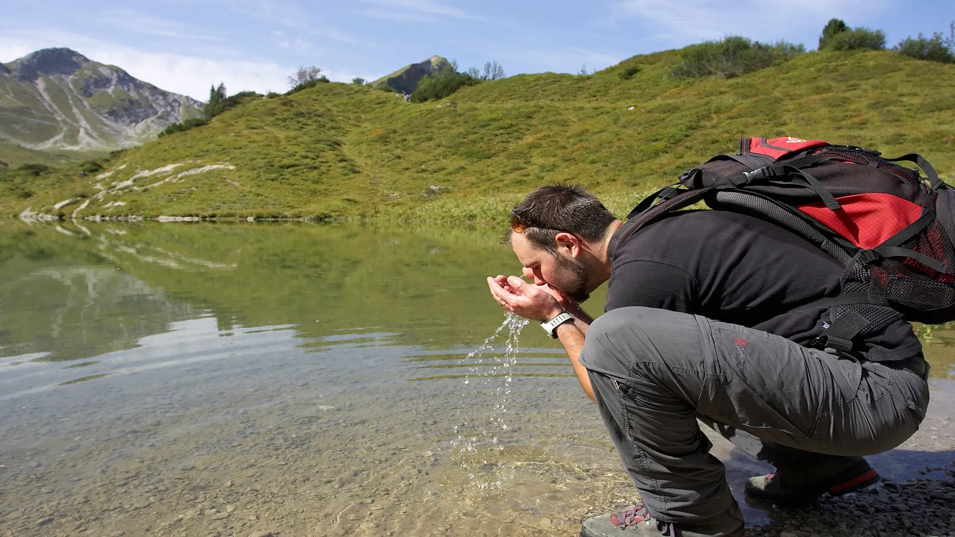 Berge voller Glück im Bäckergut - Ein Wanderer erfrischt sich an einem klaren Bergsee im Tannheimer Tal